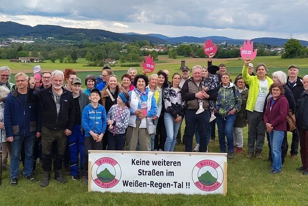 Ca. 35 Leute stehen im Talraum vor einem Banner "Keine weiteren Straßen im Weißen-Regen-Tal", 3 davon halten eine rote Hand hoch mit der Aufschrift "Hands off Nature"
