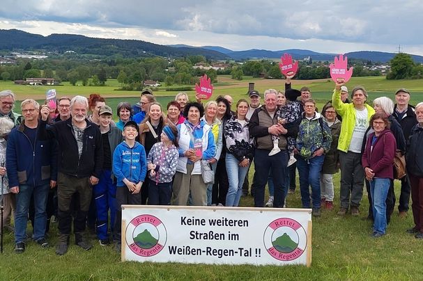 Ca. 35 Leute stehen im Talraum vor einem Banner "Keine weiteren Straßen im Weißen-Regen-Tal", 3 davon halten eine rote Hand hoch mit der Aufschrift "Hands off Nature"