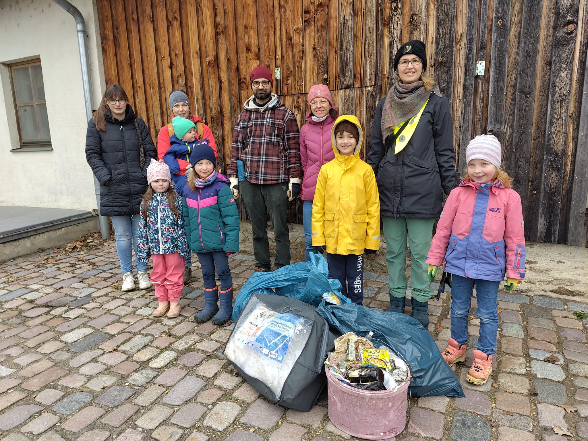Erwachsene und Kinder in wetterfester Kleidung mit Müllsäcken im Vordergrund 