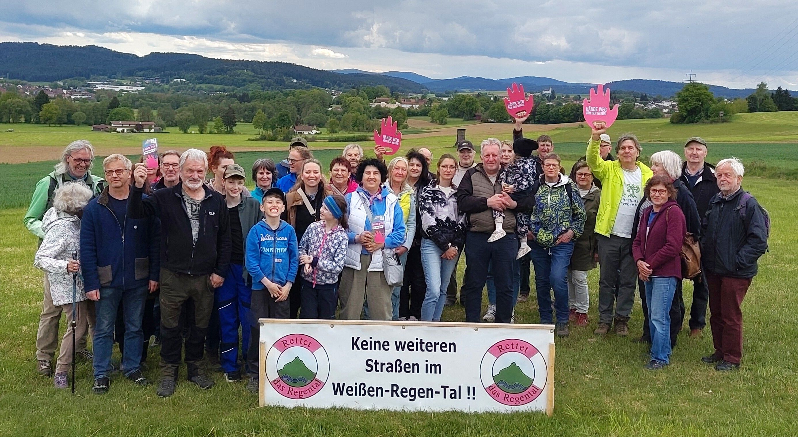 Ca. 35 Leute stehen im Talraum vor einem Banner "Keine weiteren Straßen im Weißen-Regen-Tal", 3 davon halten eine rote Hand hoch mit der Aufschrift "Hands off Nature"